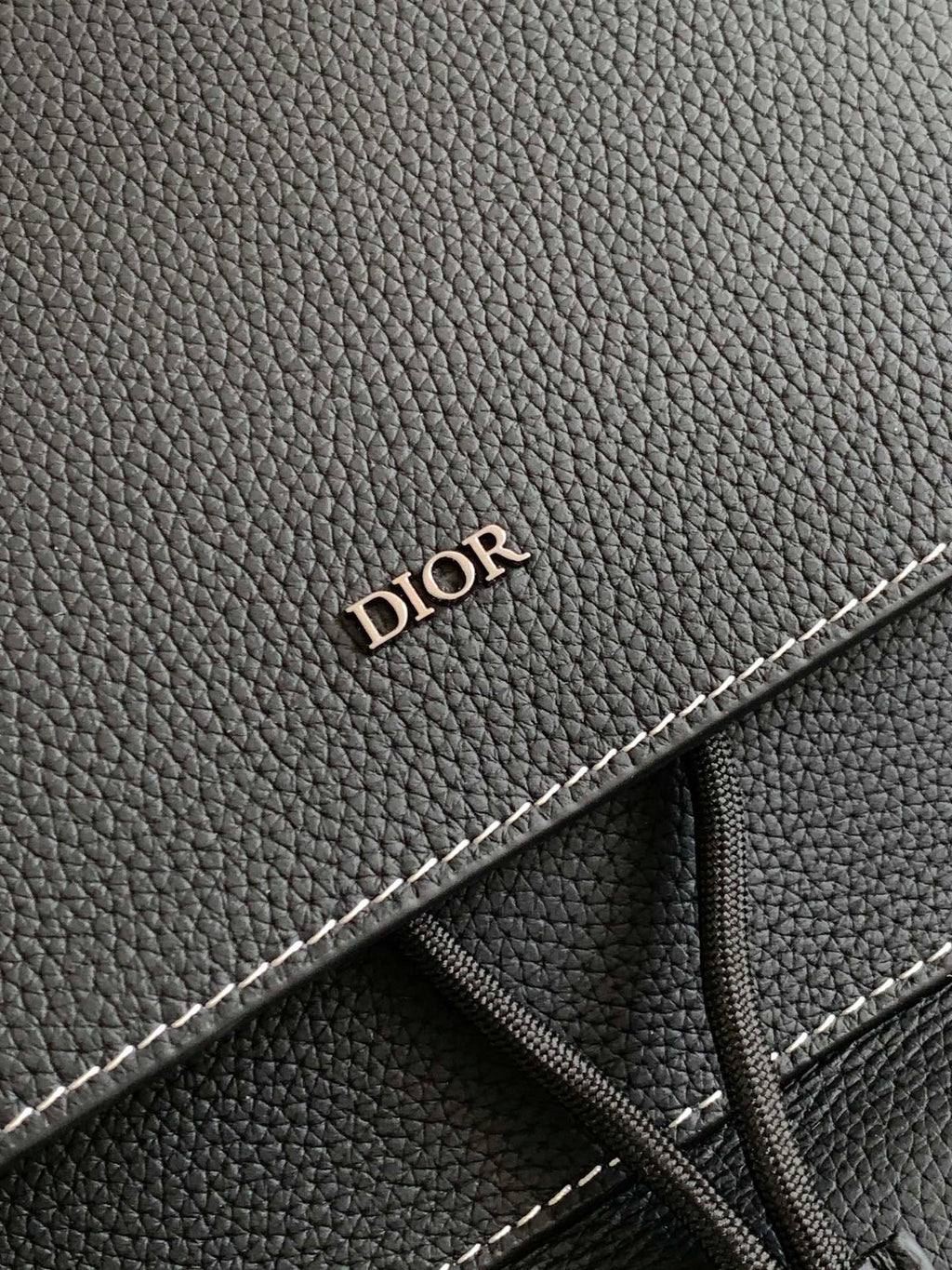 Black leather backpack detail with “DIOR” embossing and contrast stitching
