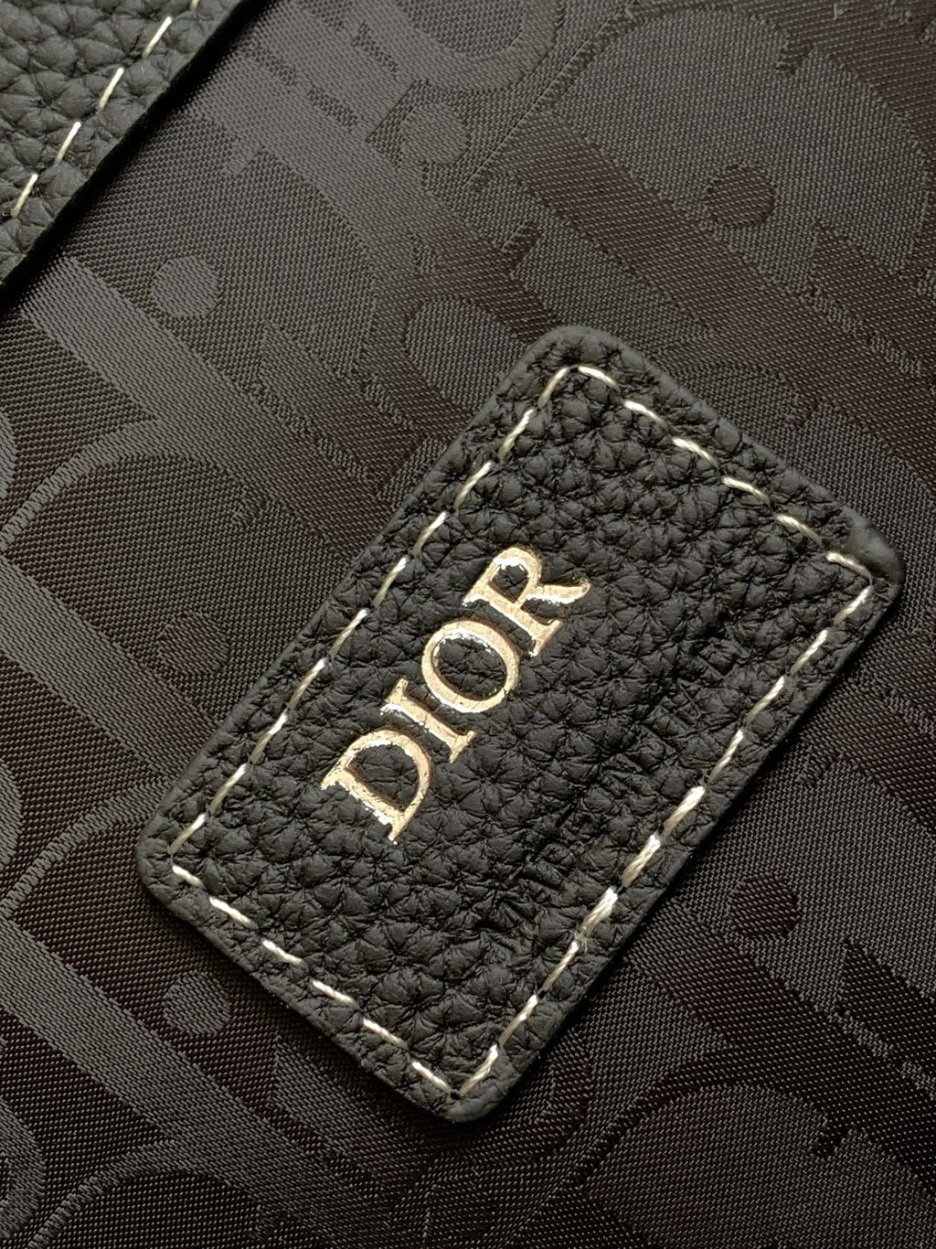 Black monogram-lined backpack panel with “DIOR” label on a stitched leather patch