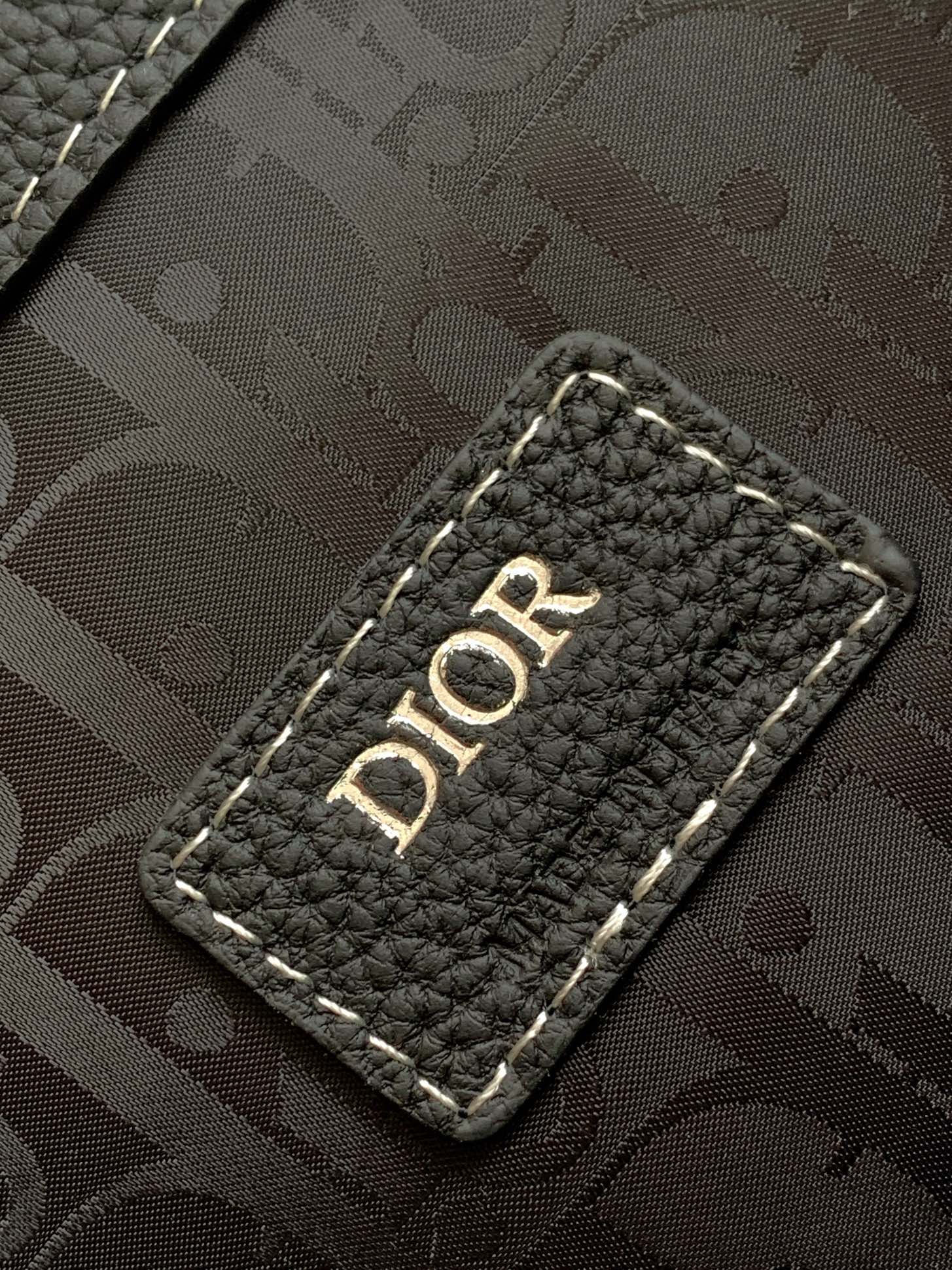Black monogram-lined backpack panel with “DIOR” label on a stitched leather patch