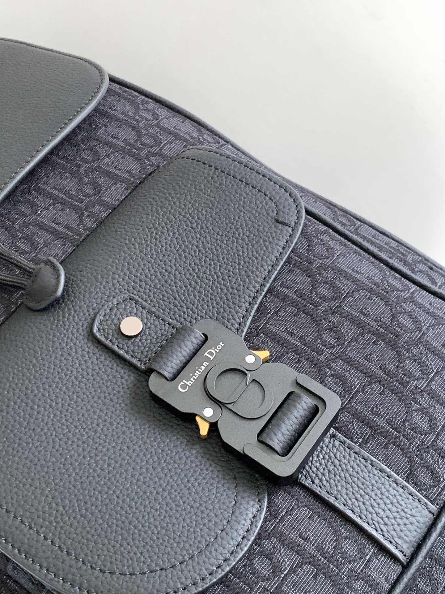 Dior men’s monogram backpack close-up of leather flap, hardware buckle, and logo charm