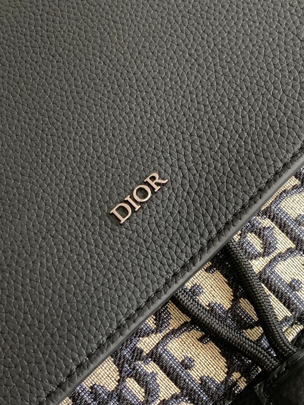 Dior backpack close-up of black leather panel with Dior logo on textured grain