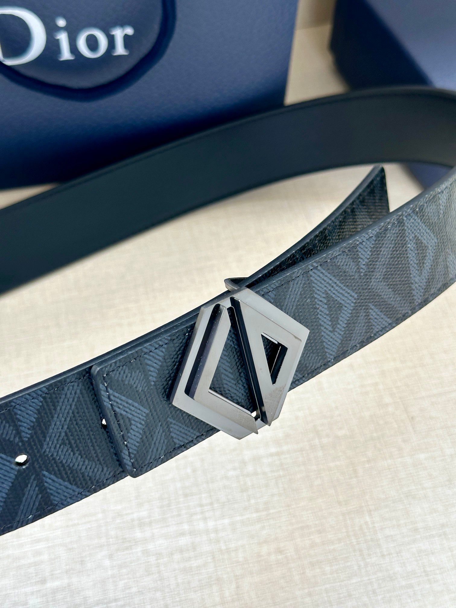 Belt buckle detail: silver-tone geometric D on dark blue patterned strap