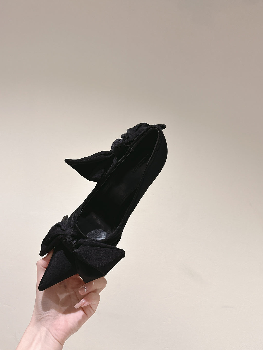 Black pointed-toe heeled sandal with bow detail held by hand