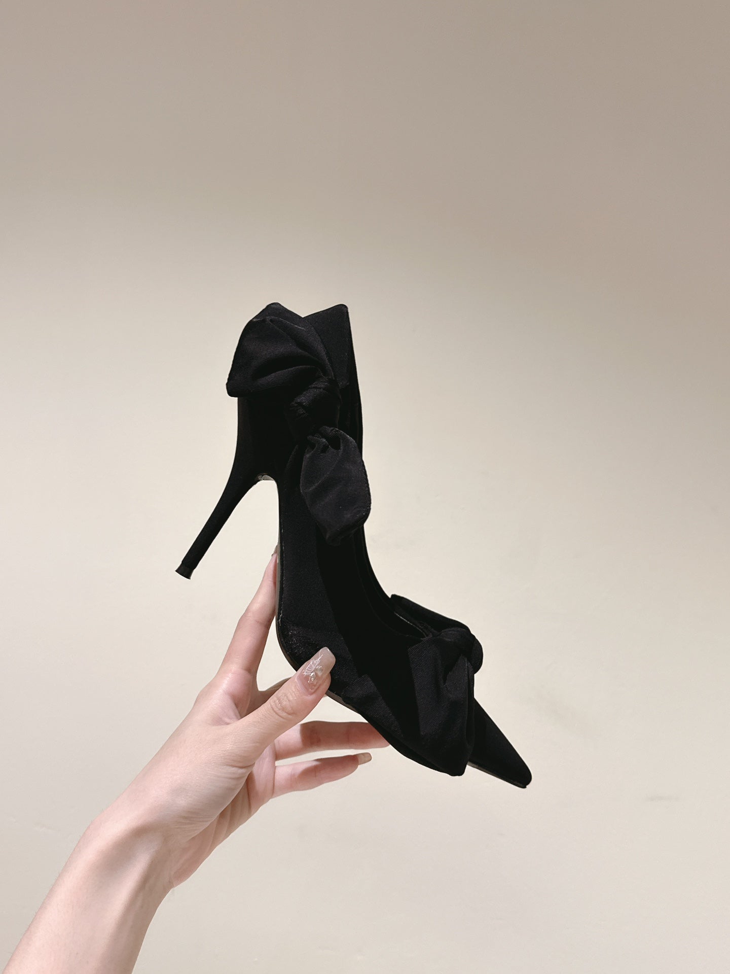 Single black bow-tied heeled sandal with slim stiletto heel held up