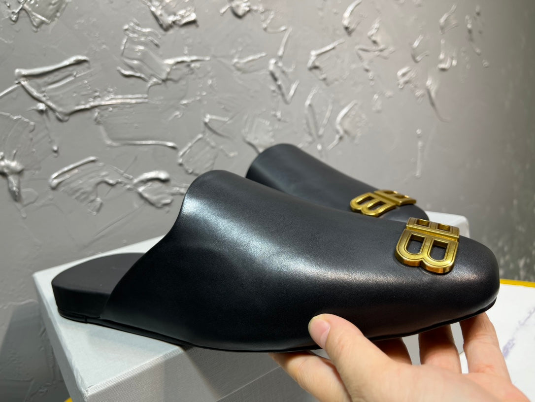 Black sandal held in hand, featuring gold BB logo on the front strap.