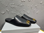 Black slip-on sandals with gold BB logo on the outer front strap.
