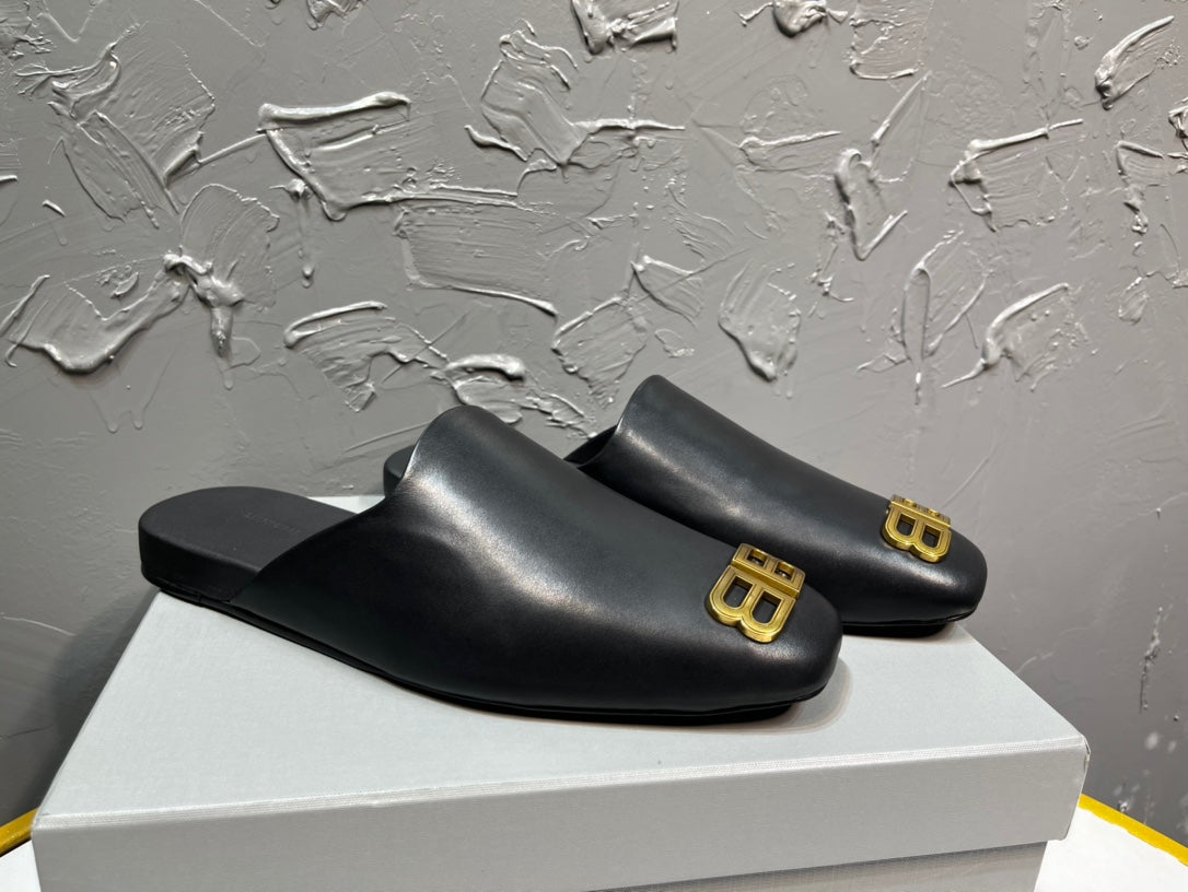 Black slip-on sandals with gold BB logo on the outer front strap.