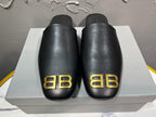 Black Balenciaga slide sandals with gold BB logo on front straps.