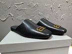Black leather slide sandals with gold B-logo ornament on upper, curved vamp