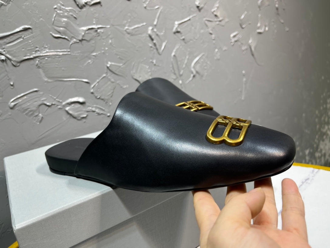 Black leather slide sandal with gold B-logo on upper, held for display