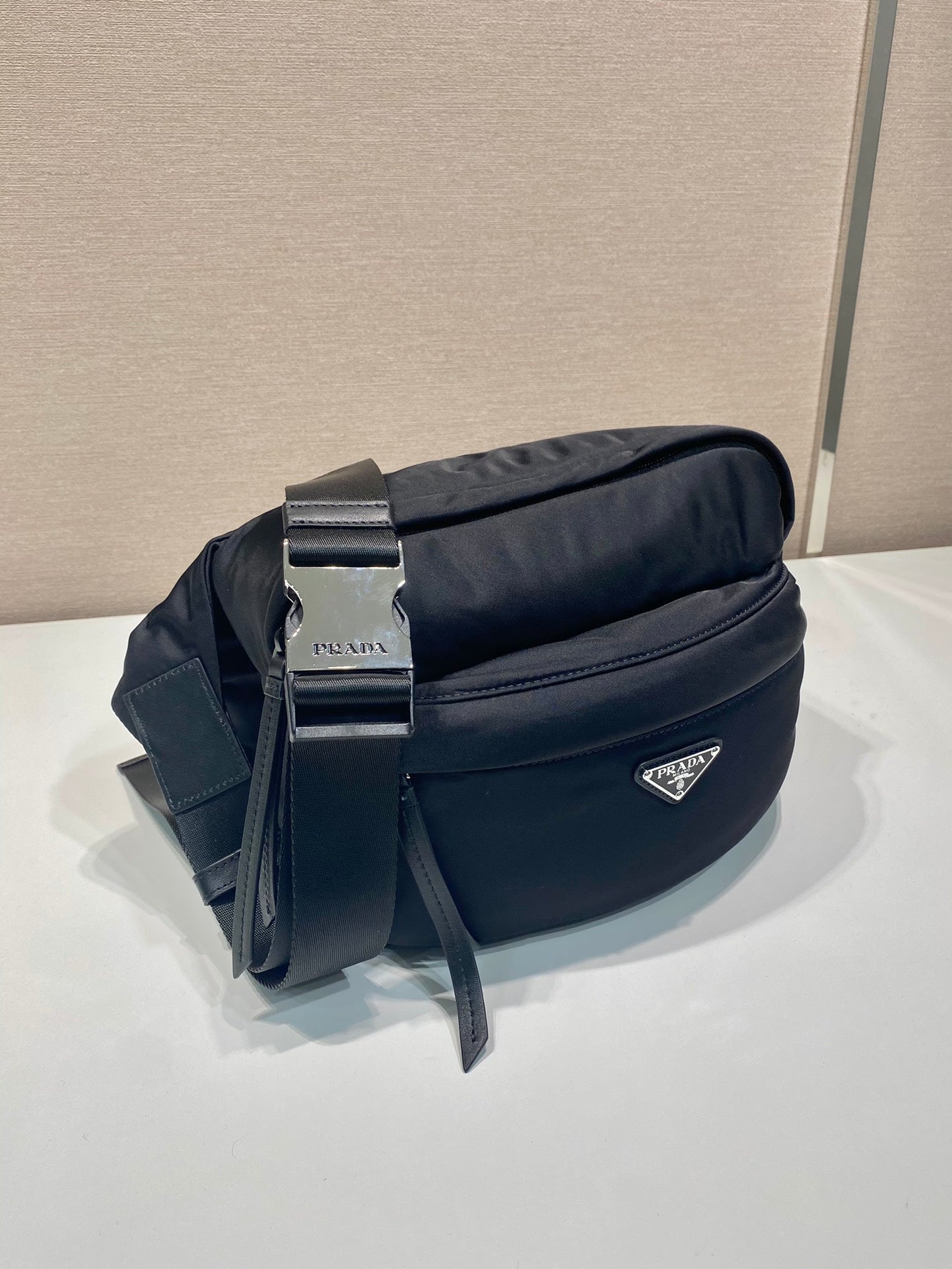 Prada black crossbody bag with silver buckle, front pocket, and hanging strap