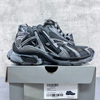 Low-top lace-up sneakers on a box, with gray-blue mesh, silver overlays, and thick rubber sole