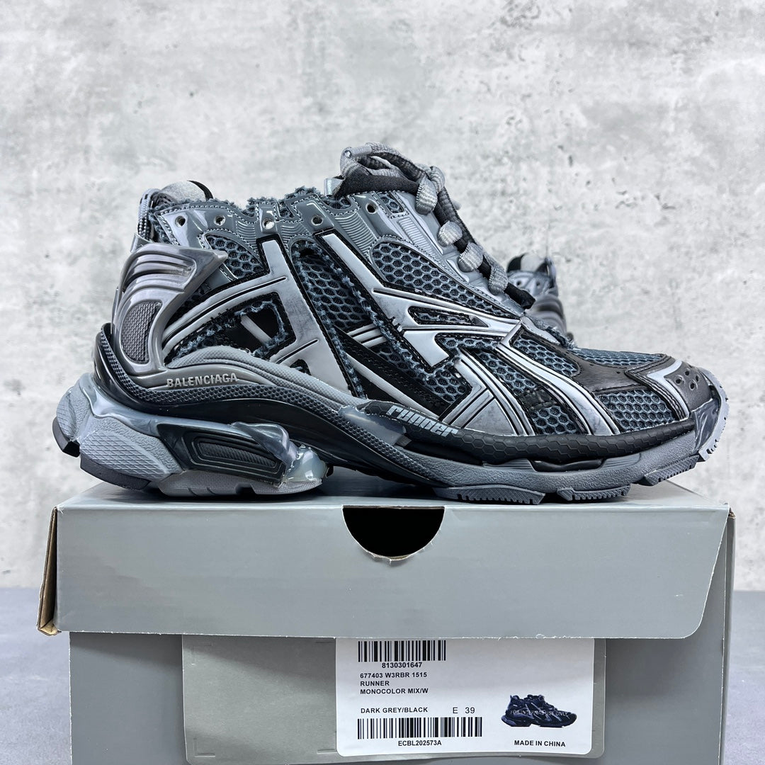 Low-top lace-up sneakers on a box, with gray-blue mesh, silver overlays, and thick rubber sole