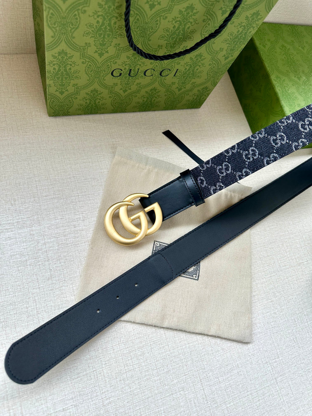 Gucci belt laid flat: dark navy GG strap with gold-tone double-G buckle