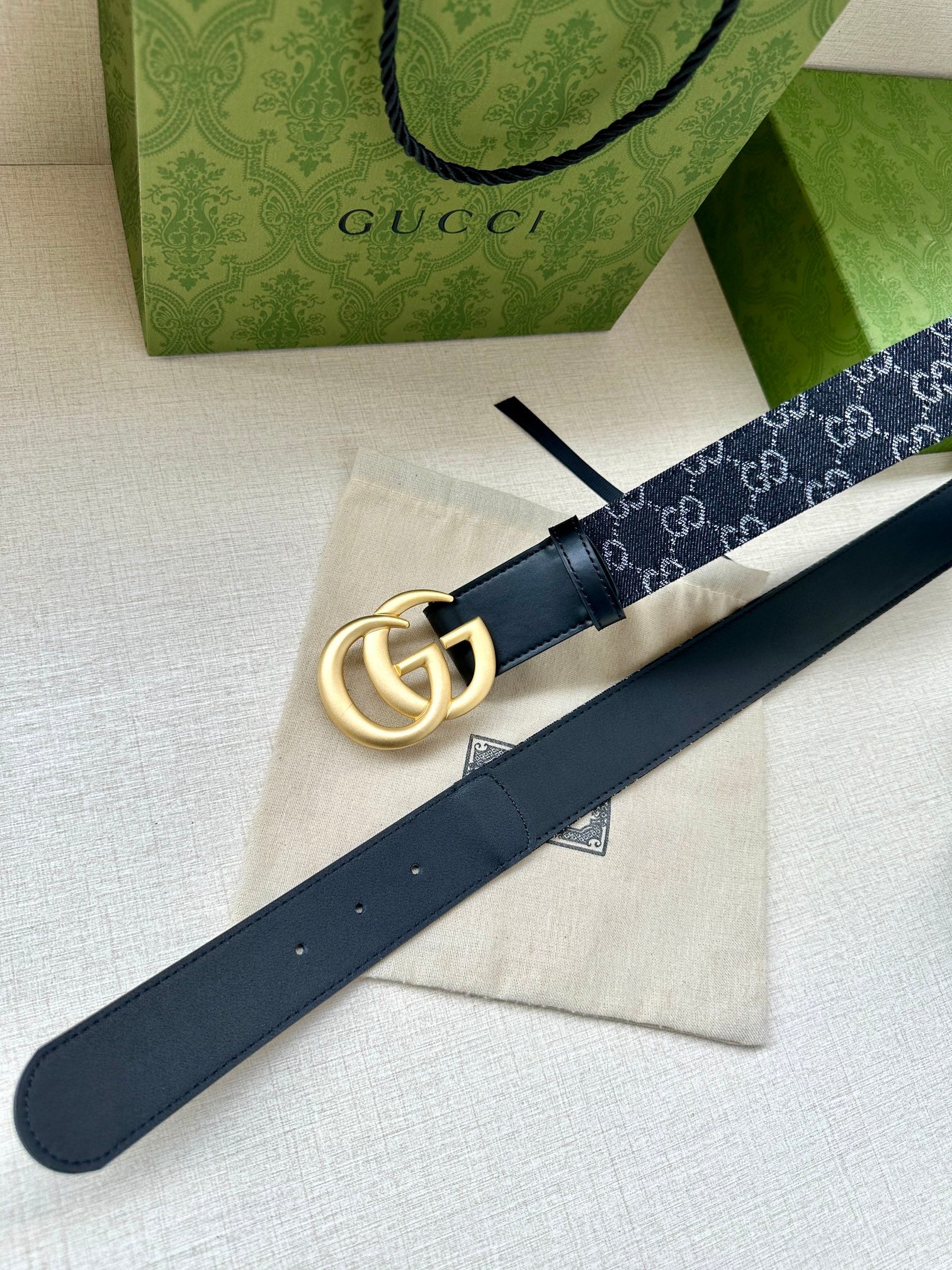 Gucci belt laid flat: dark navy GG strap with gold-tone double-G buckle