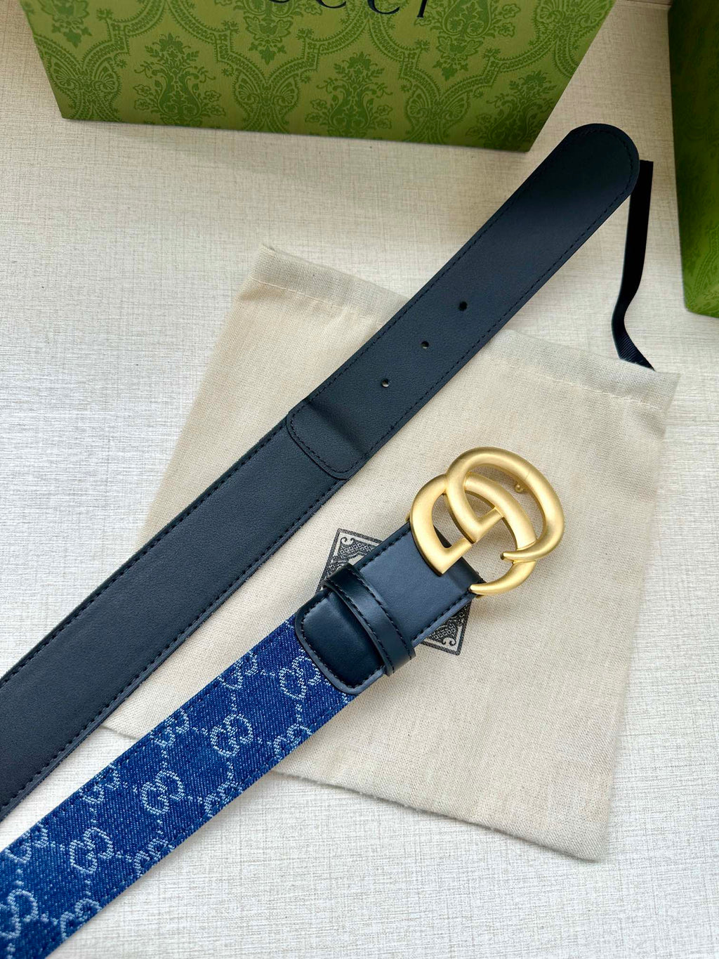 Gucci belt detail: dark blue monogram strap with navy leather backing and gold GG buckle.
