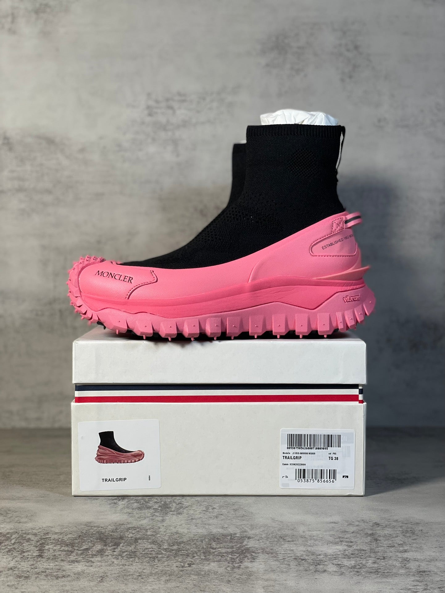 Sock boot sneaker with black knit ankle and pink lug sole on box.