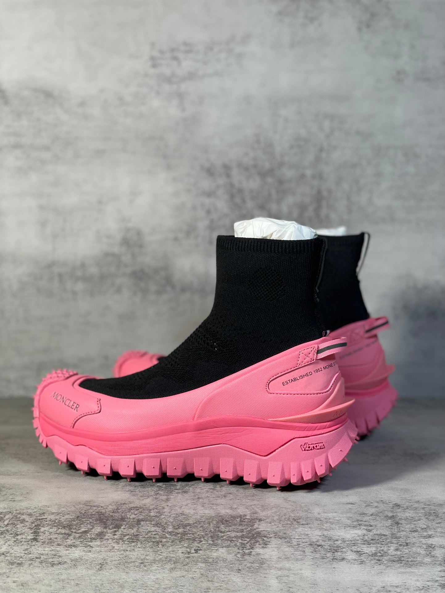 Sock boot sneaker with black knit upper, pink side panel and studded lug sole.