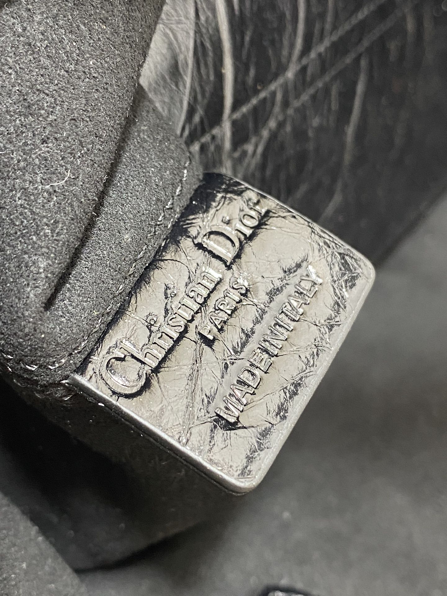 Dior embossed logo on dark metallic leather corner, stitch detail