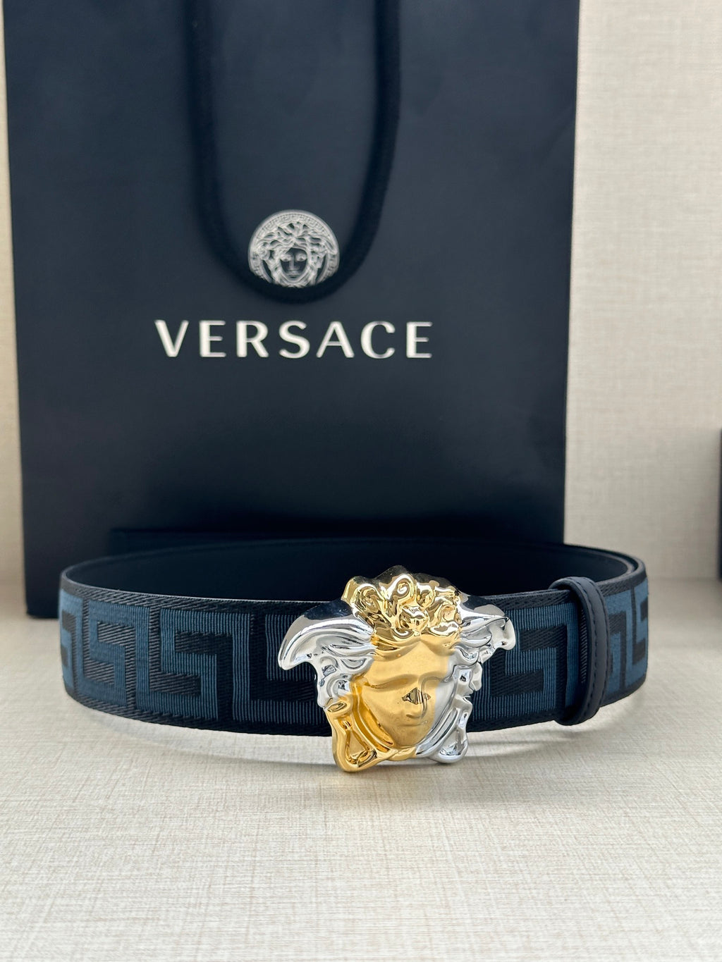 Versace belt: blue Greek-key strap with gold/silver Medusa head buckle, front view.