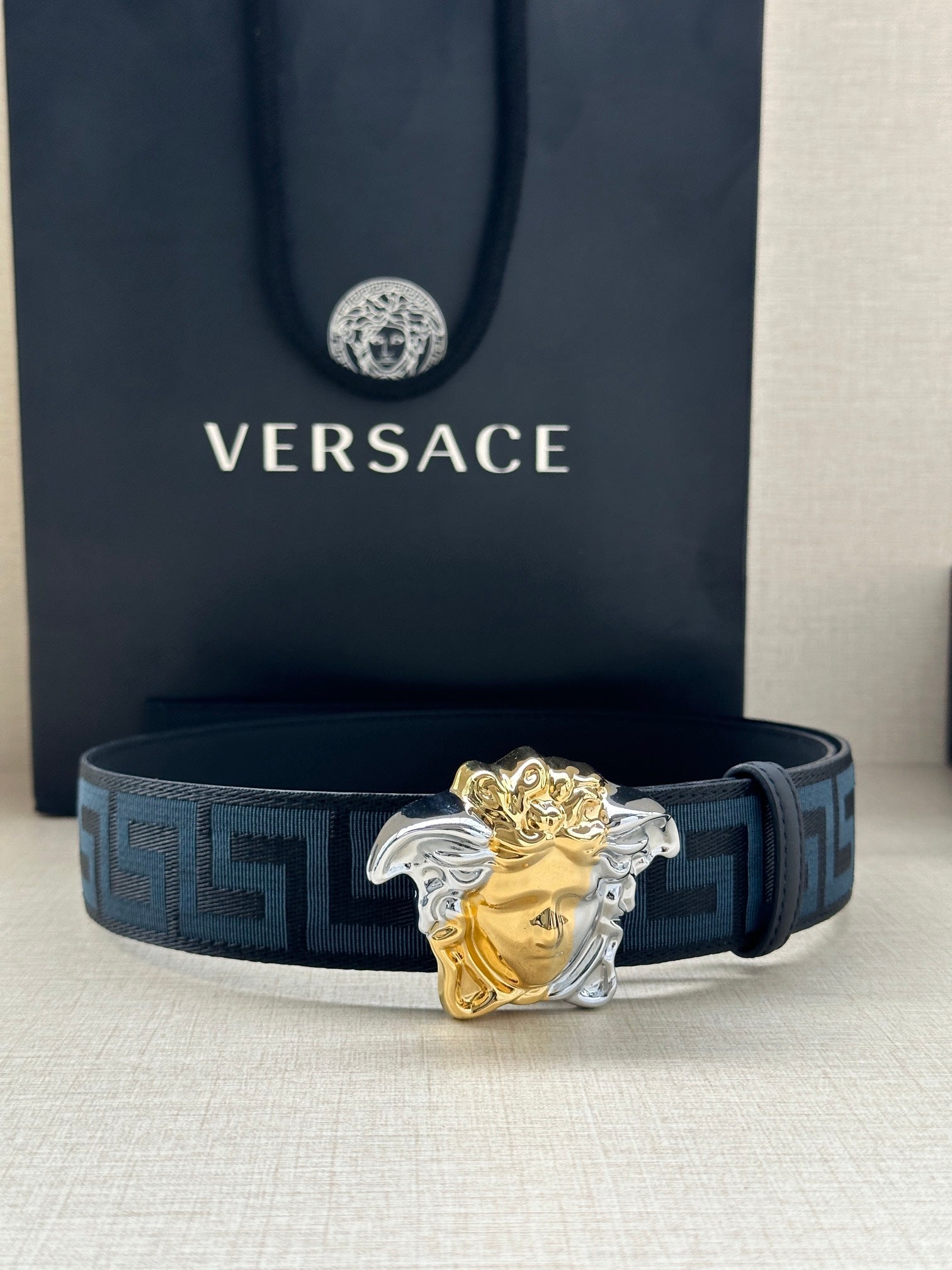 Versace belt: blue Greek-key strap with gold/silver Medusa head buckle, front view.