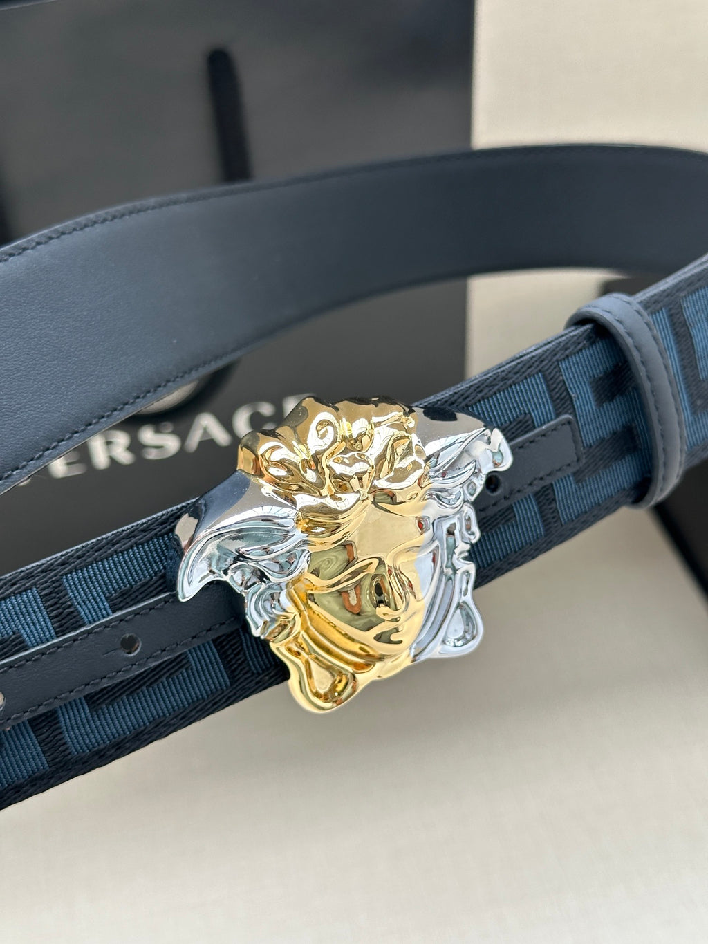 Versace belt close-up: blue Greek-key strap with gold and silver Medusa buckle.