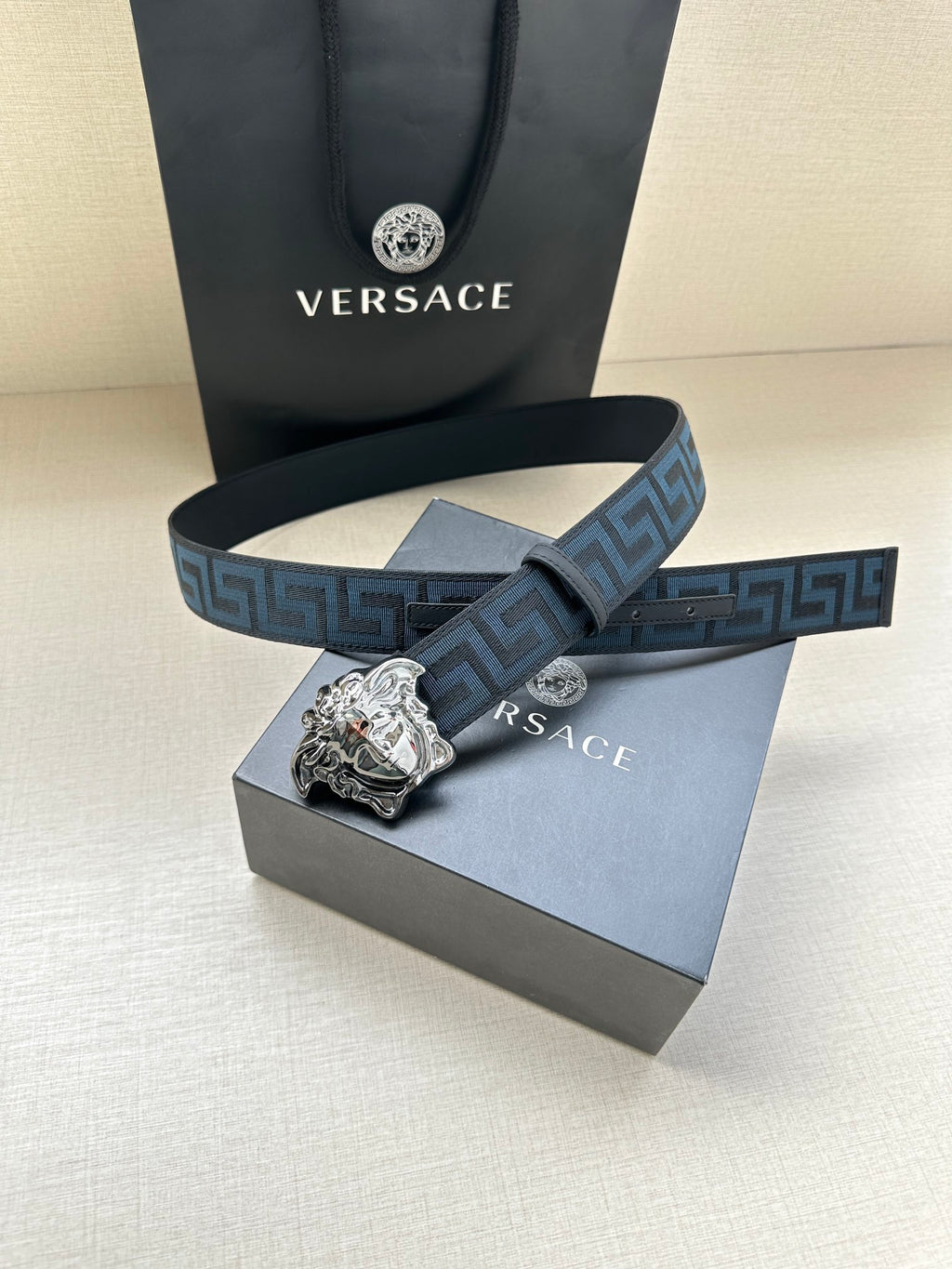 Versace belt stacked view: blue patterned strap with silver Medusa buckle, beside box.