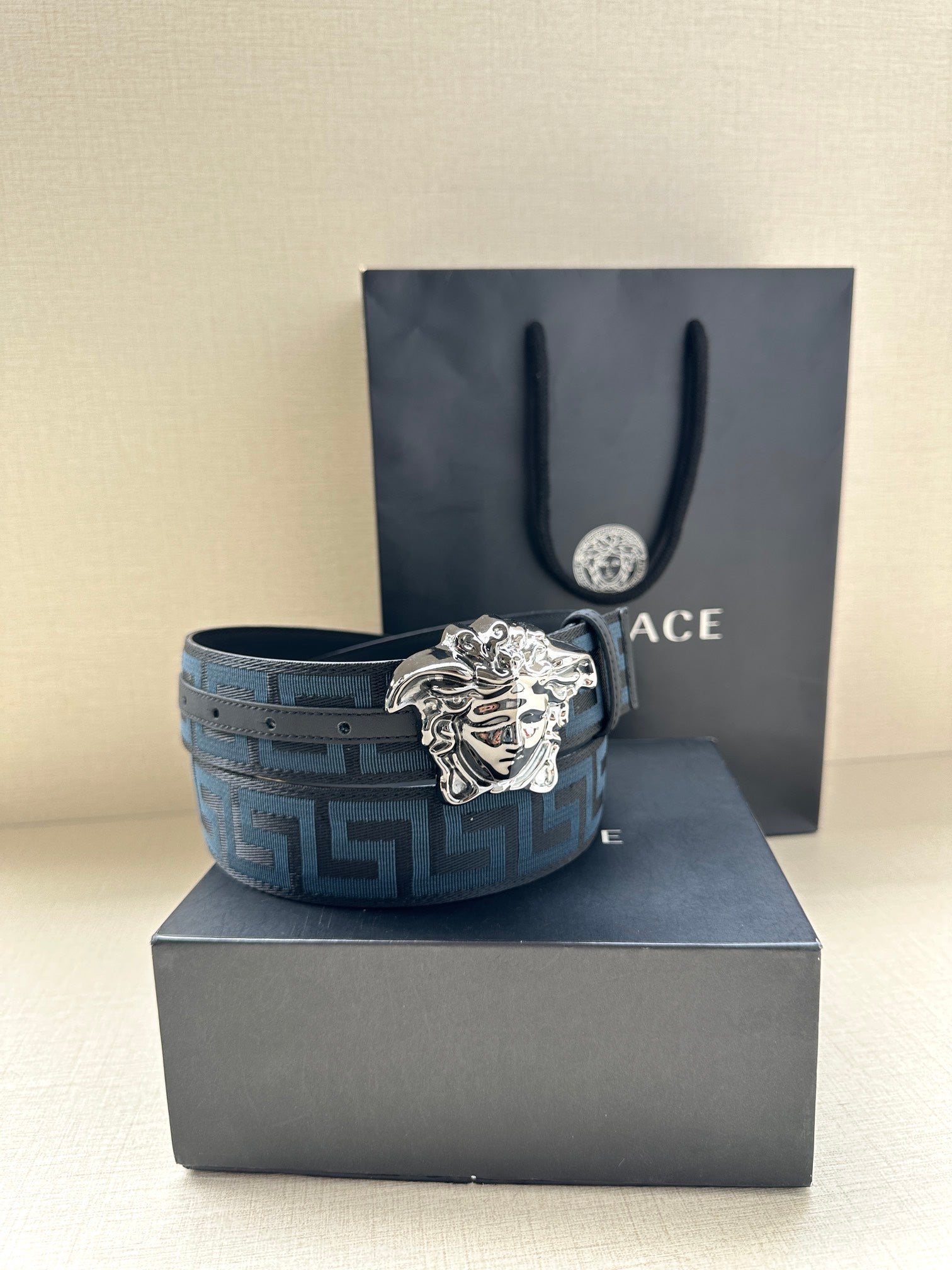 Versace belt with blue geometric pattern strap and silver Medusa buckle on box.