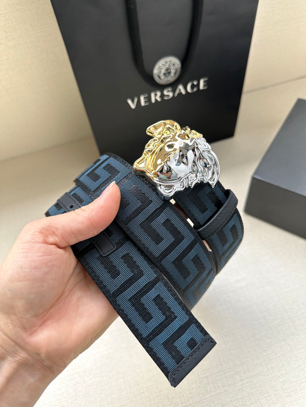 Hand-held view of dark blue Greca belt with gold and silver Medusa buckle