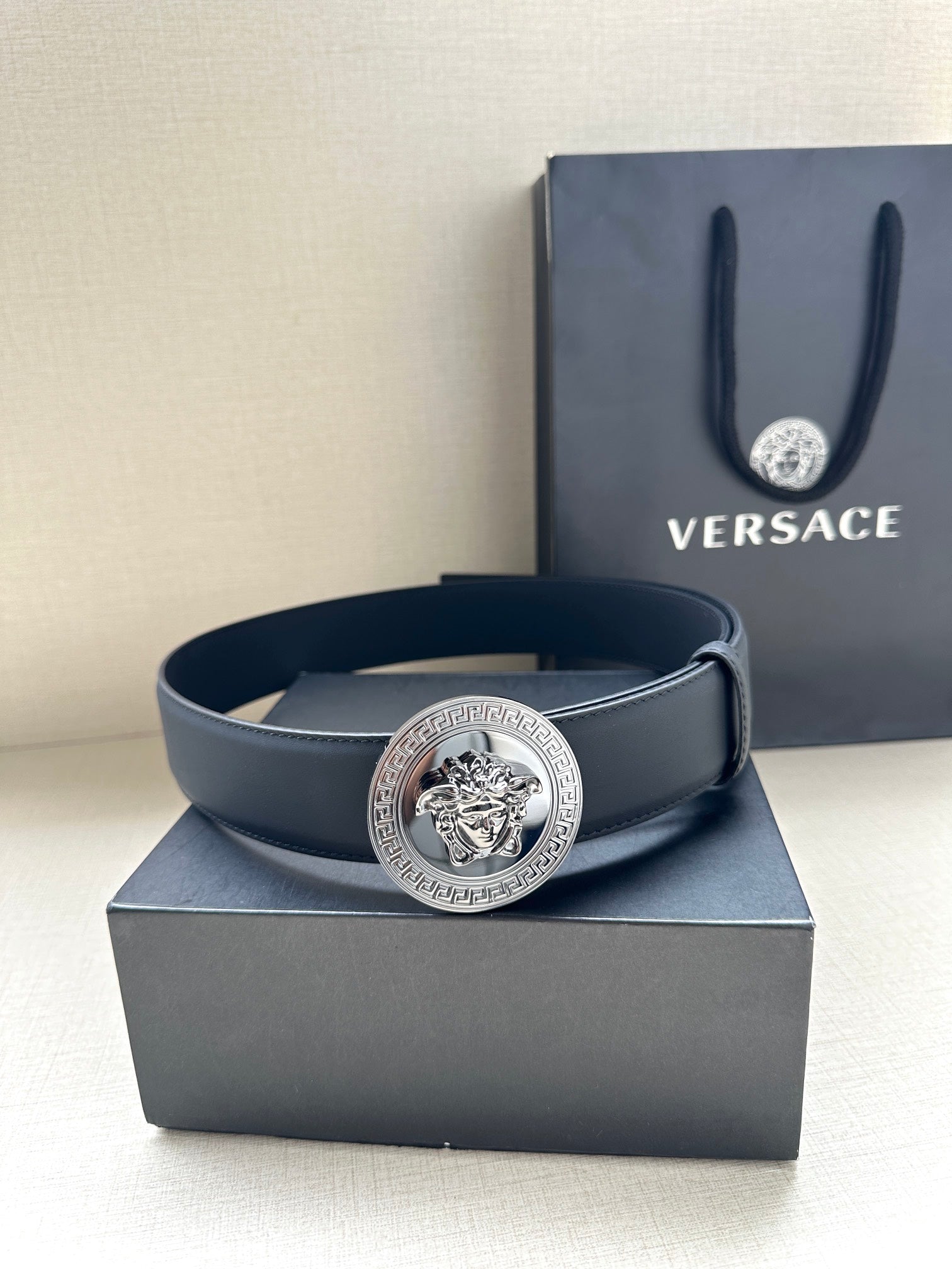 Navy leather belt with round silver medallion buckle, shown on box