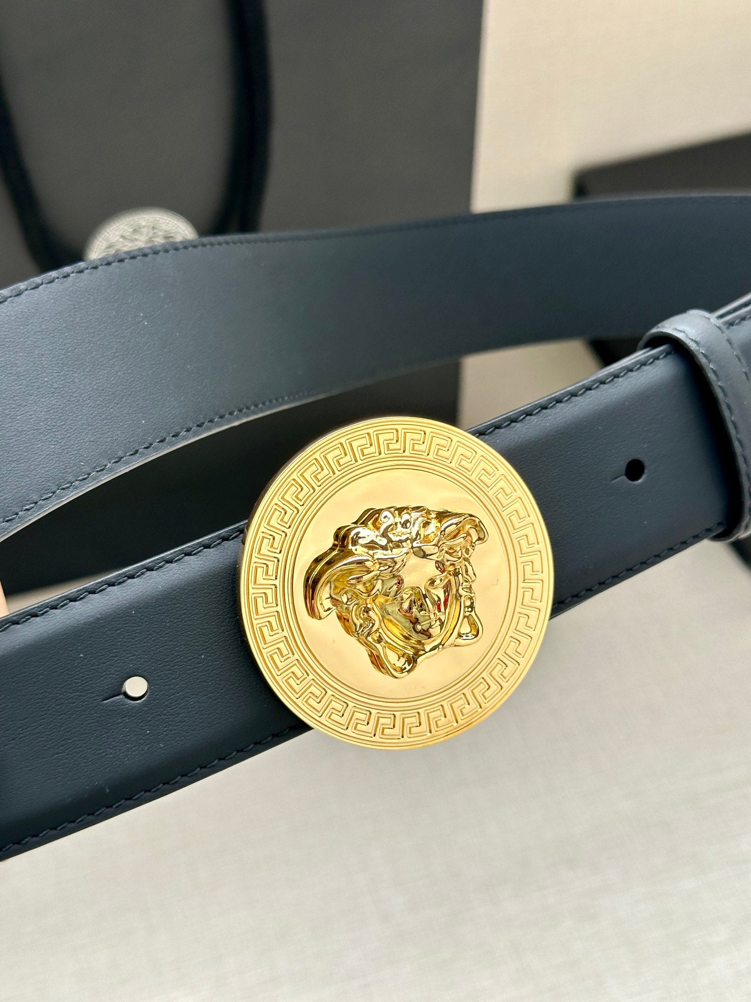 Navy leather belt with gold medallion buckle, close-up of circular emblem