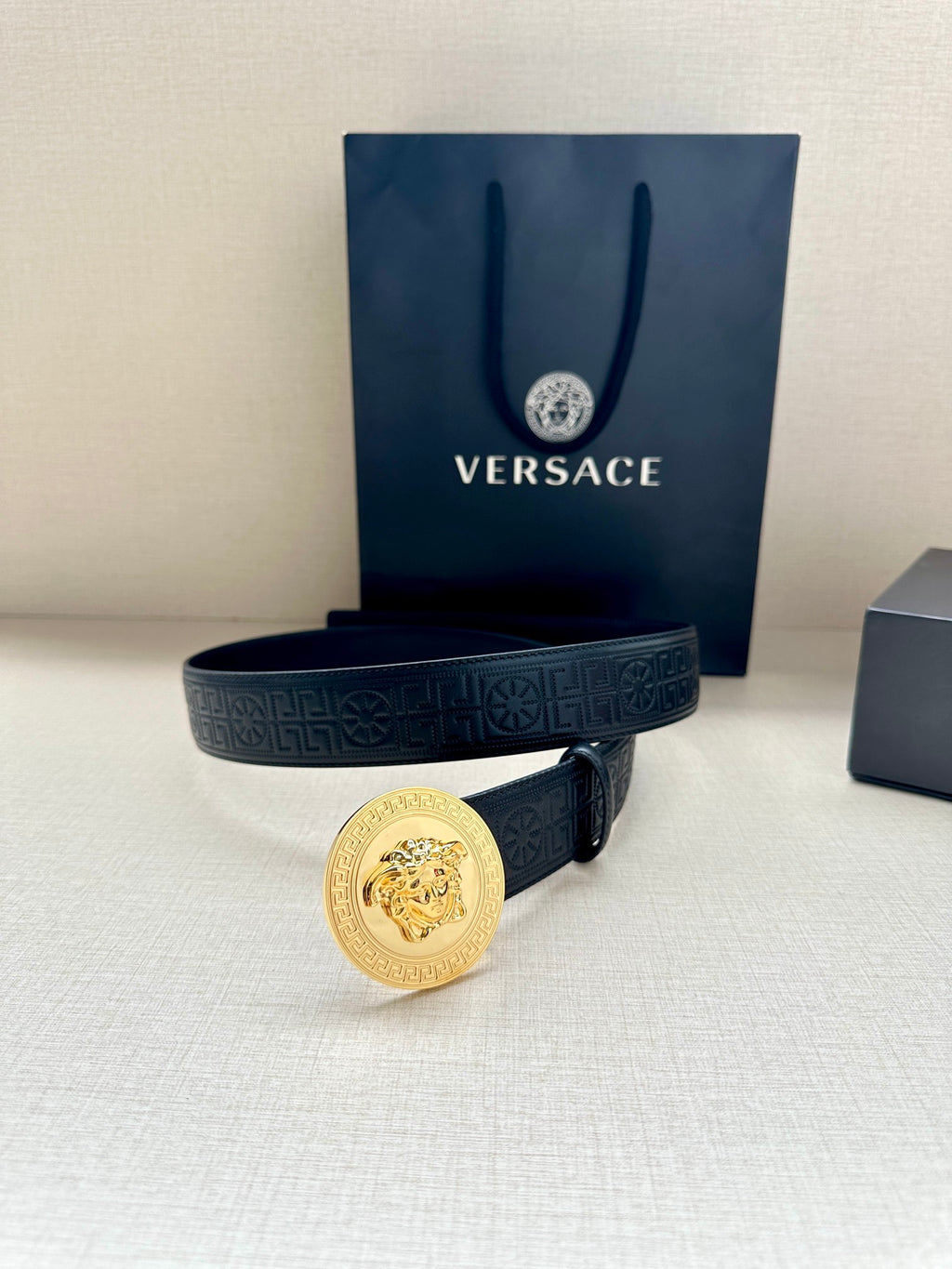 Versace belt in dark blue with gold Medusa medallion buckle, laid across boxes.