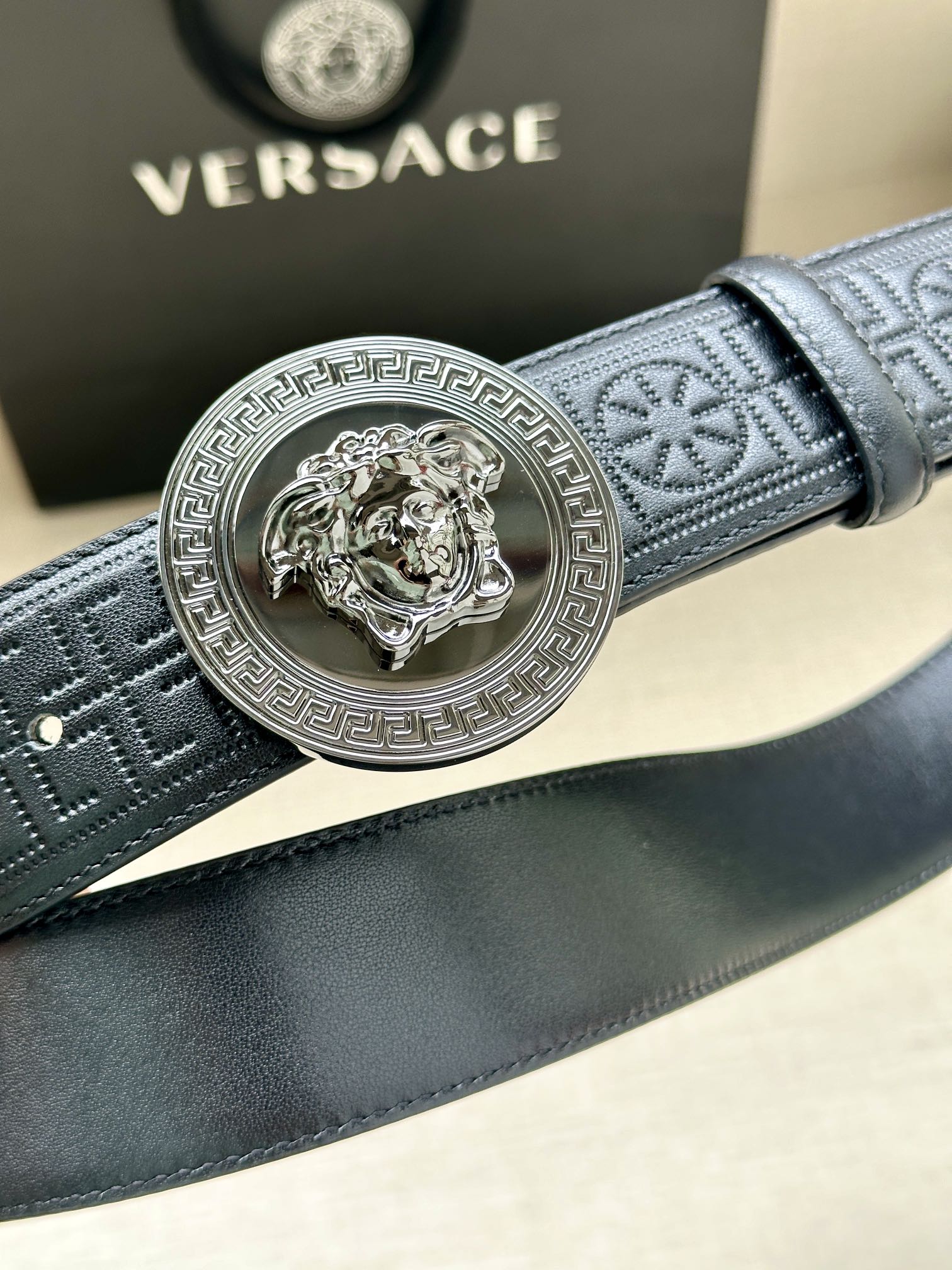Versace belt close-up: dark blue textured strap with silver Medusa medallion buckle.
