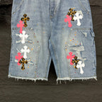 Light blue denim shorts with multicolor cross patches and chest-style pins