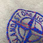 Embroidered blue Stone Island logo graphic on heather gray fabric