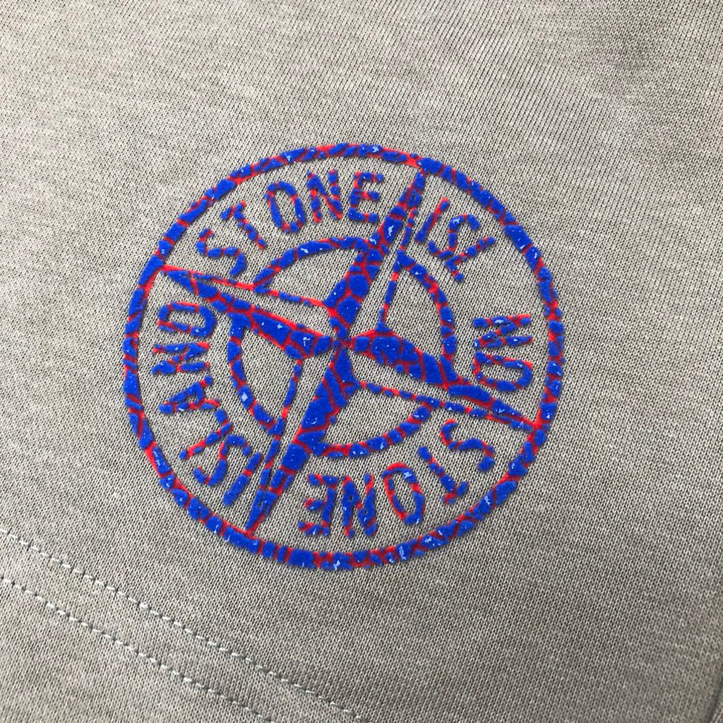 Embroidered blue Stone Island logo on light gray fabric