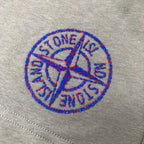 Embroidered blue Stone Island logo on light gray fabric