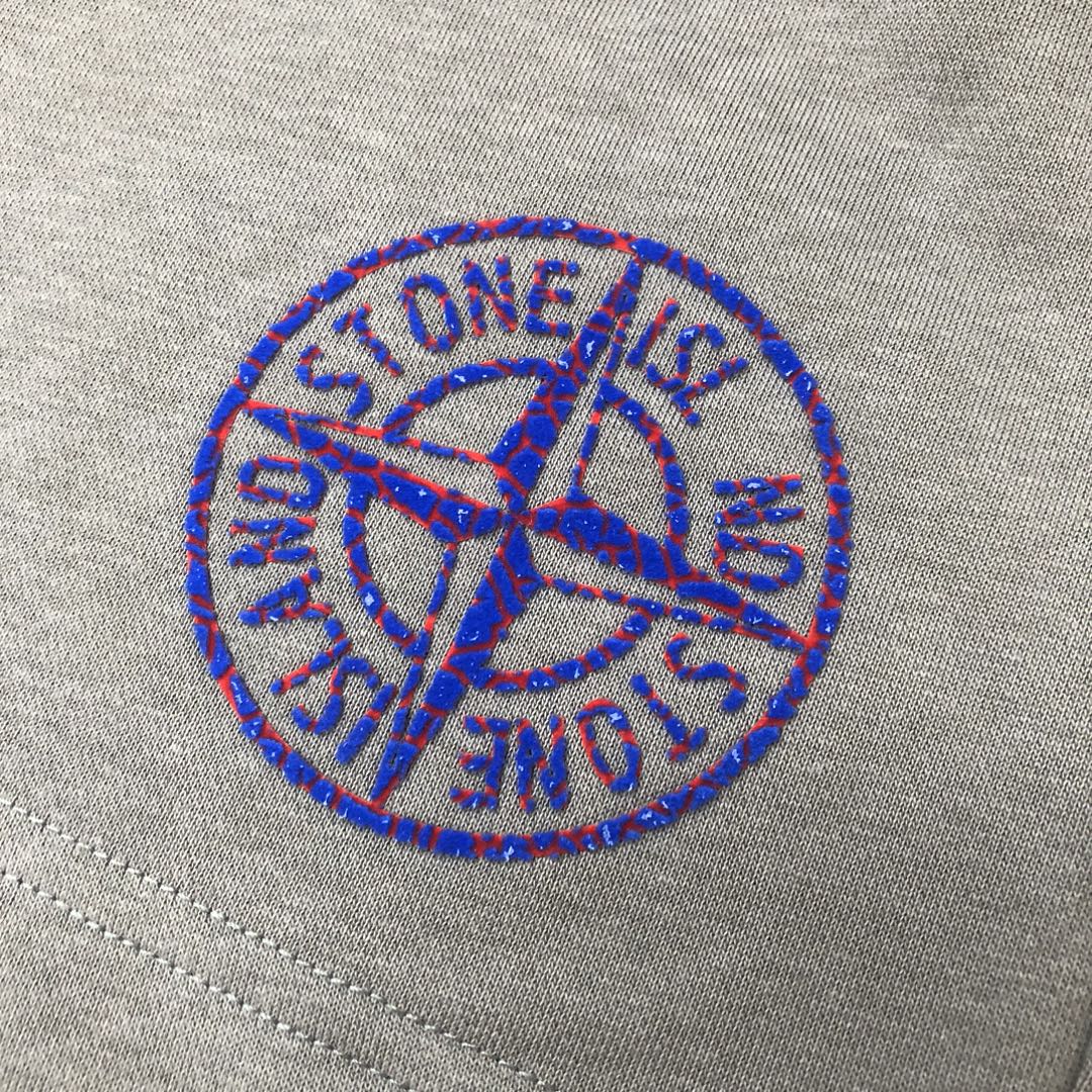 Embroidered blue Stone Island logo on light gray fabric