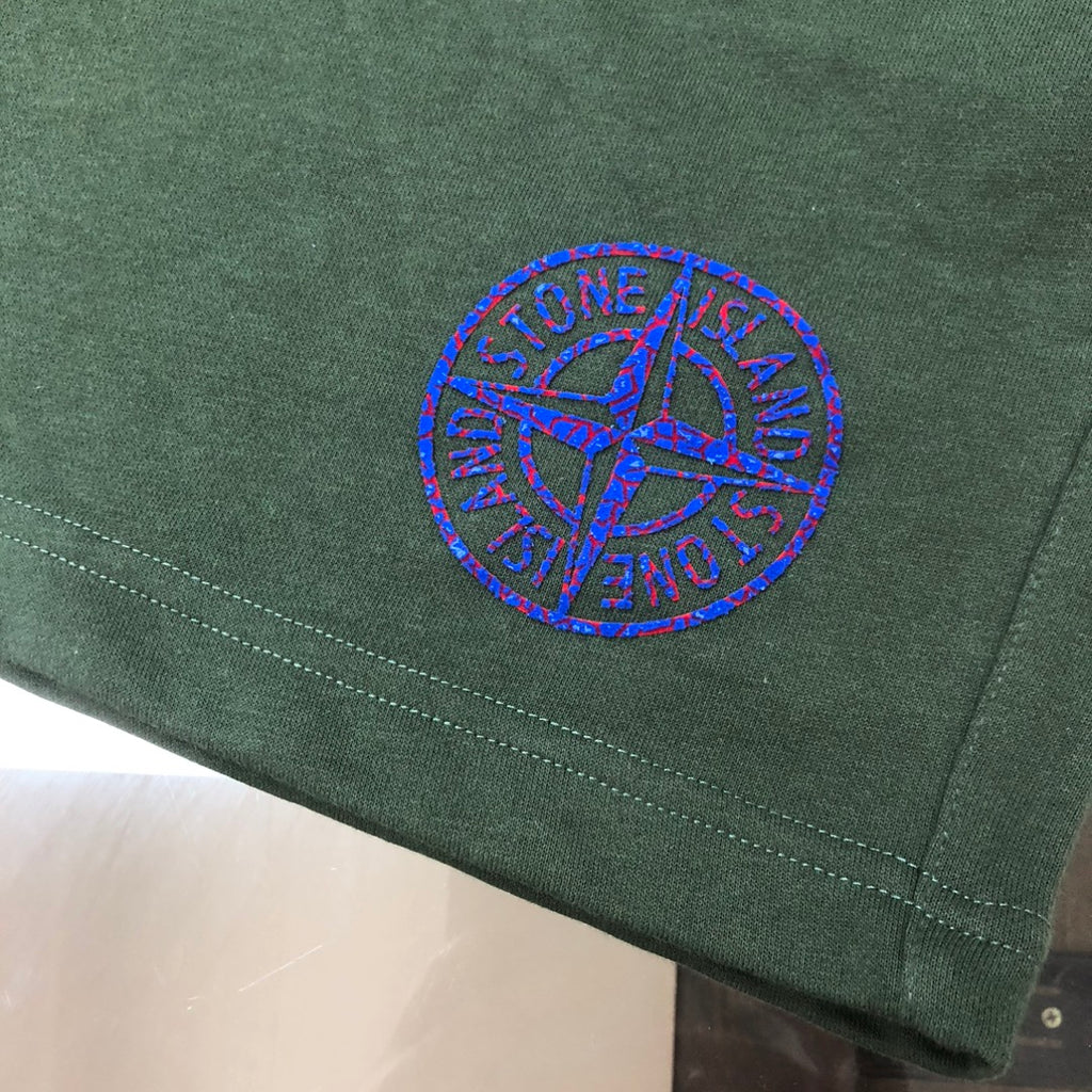 Dark green shorts front with blue circular logo embroidery near hem