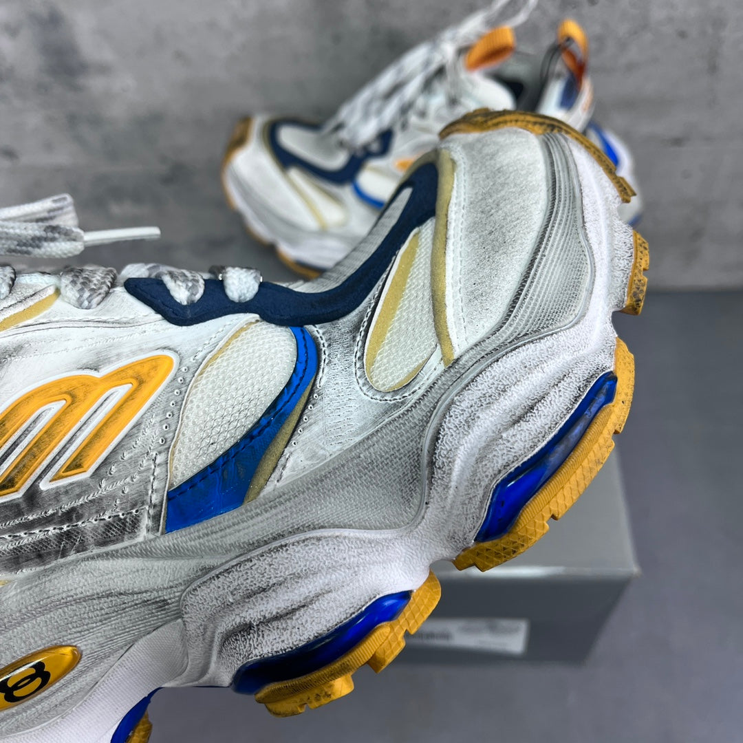 Balenciaga unisex sneaker close-up showing silver suede, blue trim, and gold logo detail.