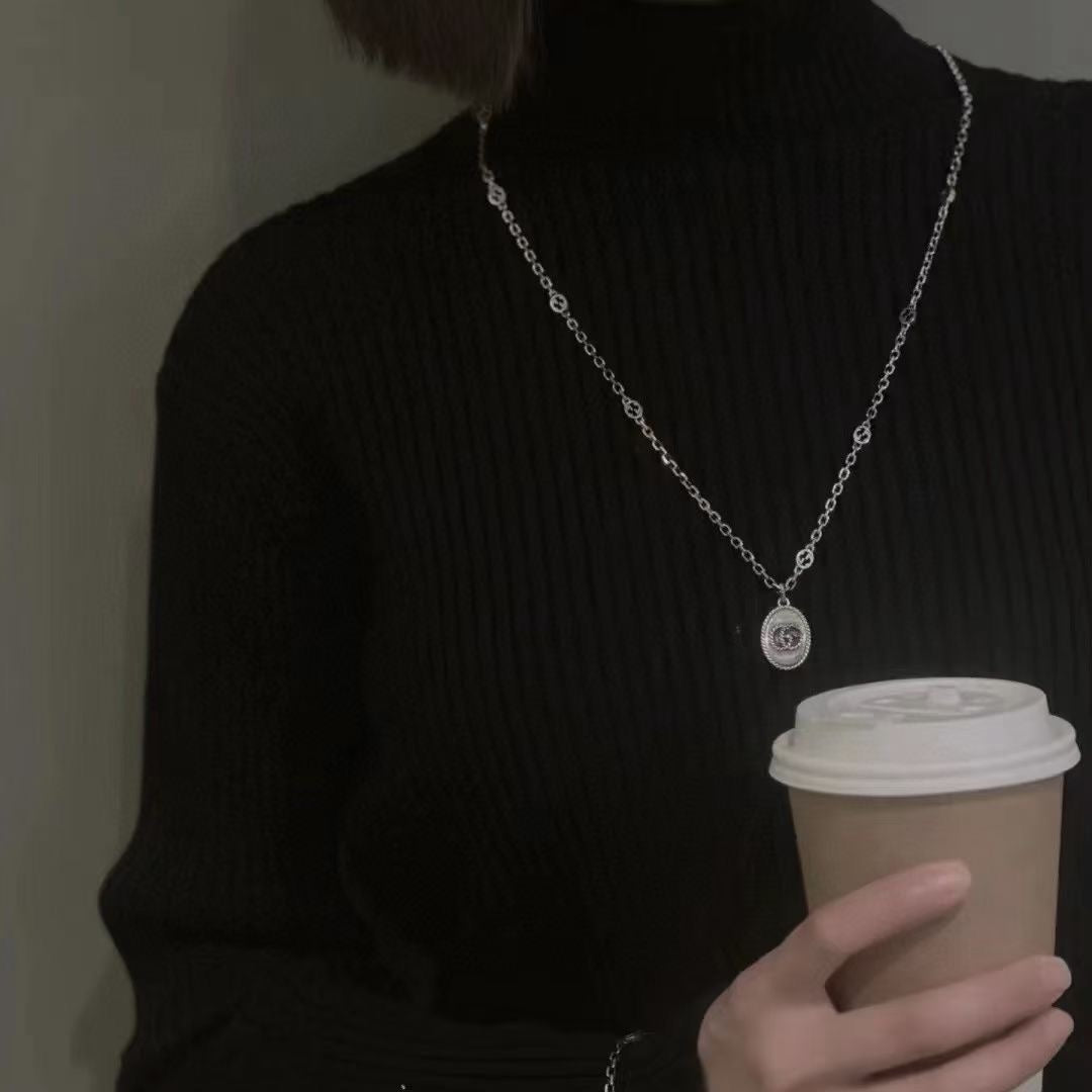 Silver chain necklace with oval logo pendant on black sweater