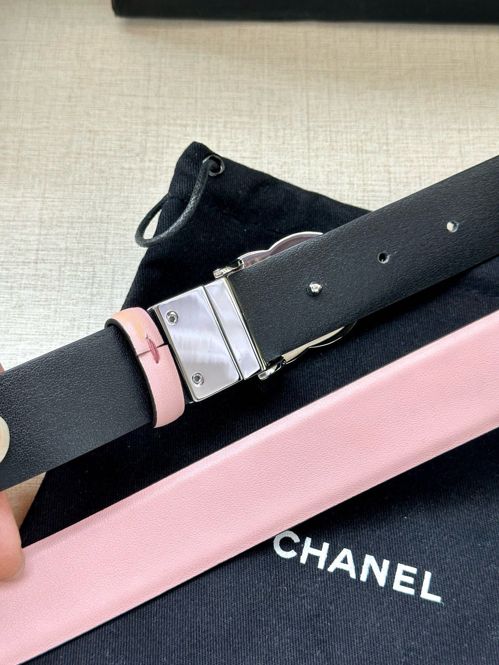 Chanel belt close-up with pale pink strap and silver-tone buckle on dark lining