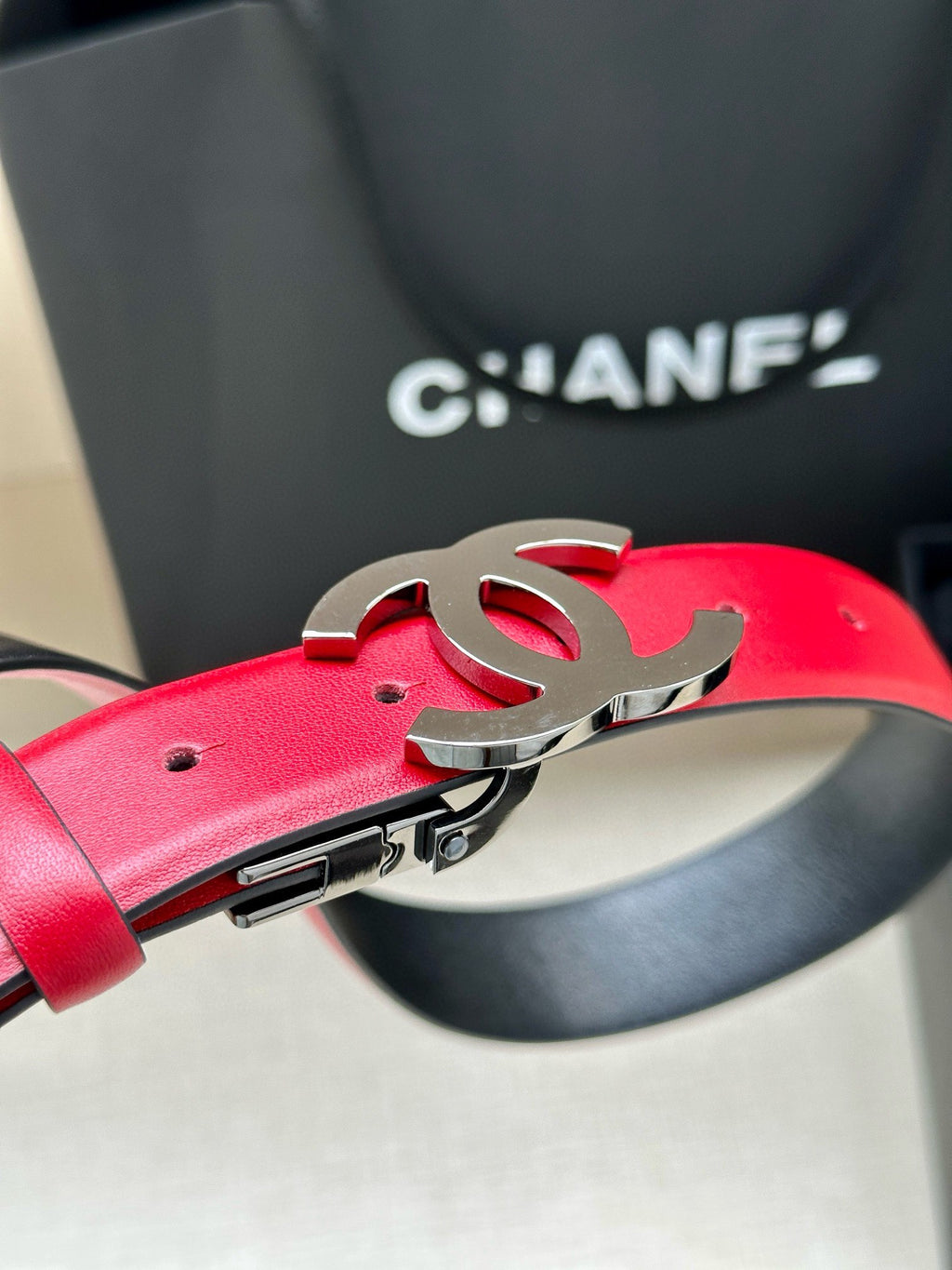 Red leather Chanel belt close-up with silver-tone buckle and metal clasp.