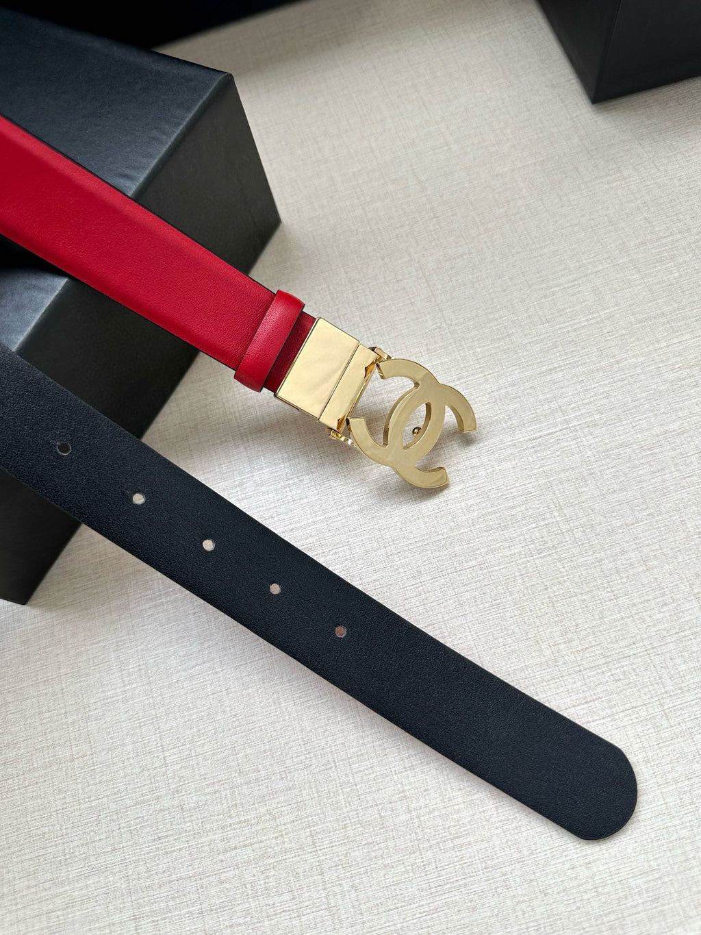 Red leather Chanel belt close-up with gold-tone CC buckle and strap holes.