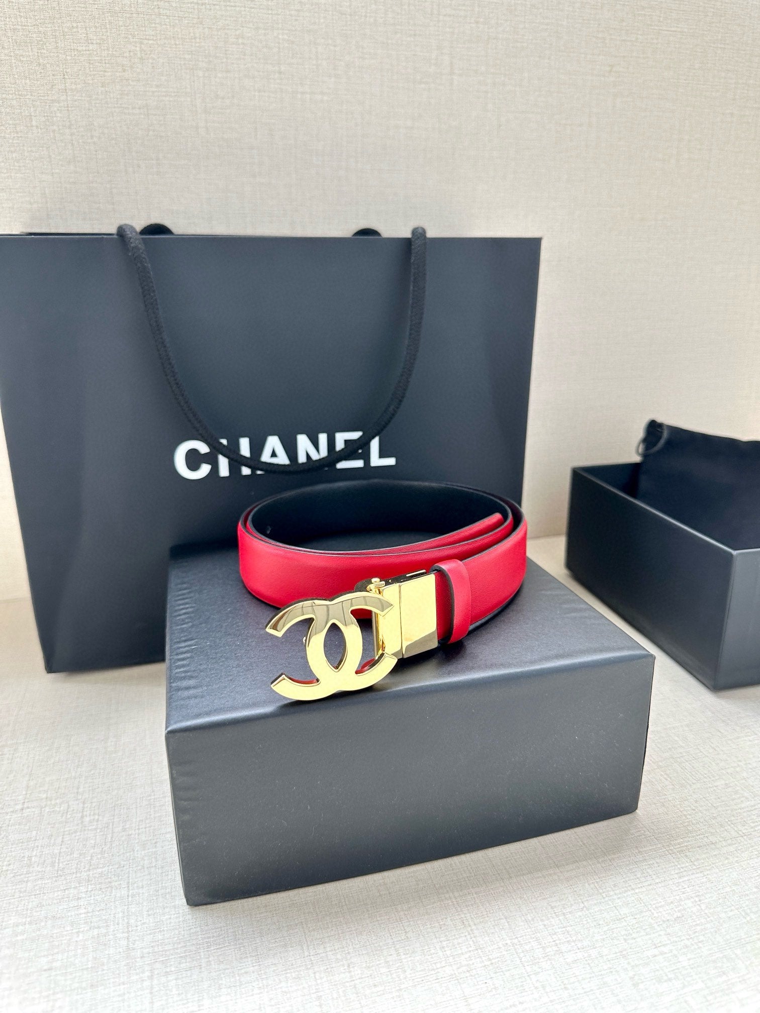Red leather Chanel belt resting on a box with a gold-tone CC buckle.