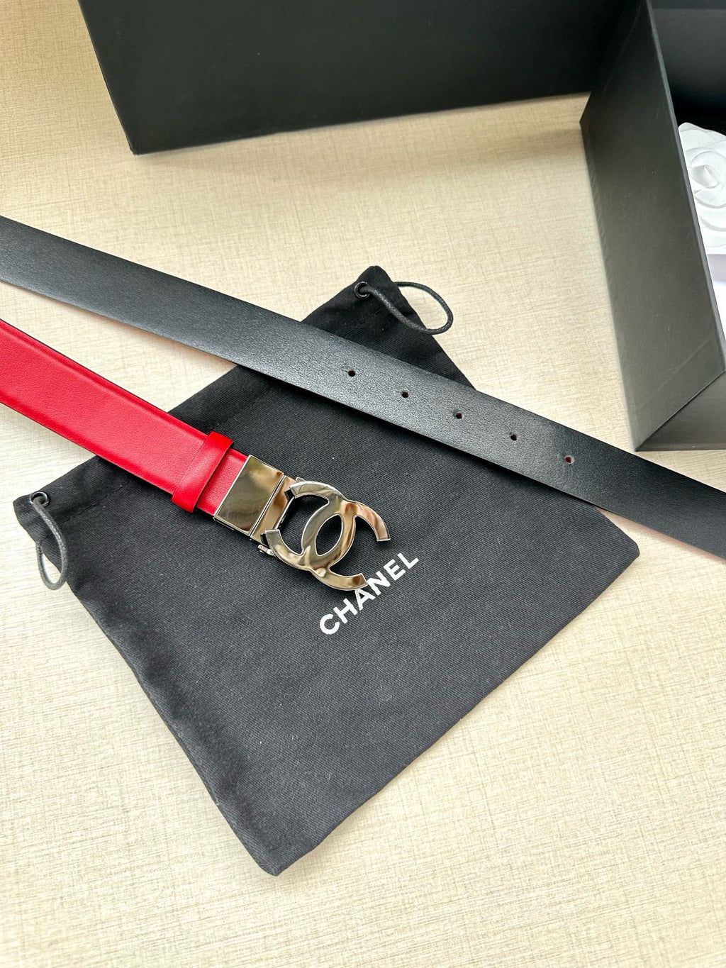 Red leather Chanel belt with silver-tone CC buckle on dark pouch.