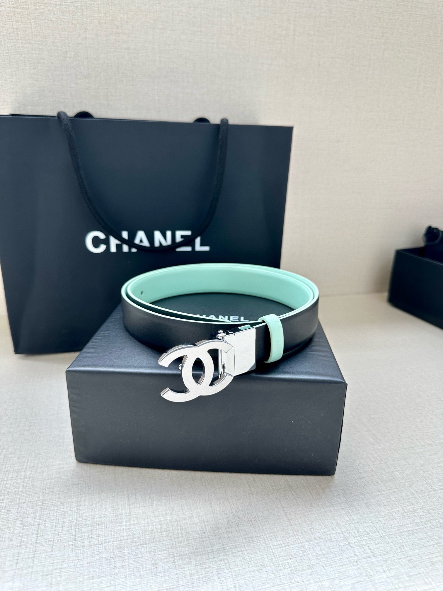 Chanel belt with light mint strap and silver CC buckle, resting on black box.