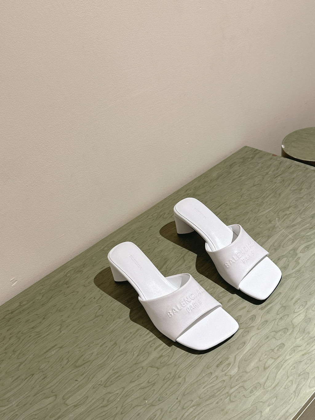 White slide sandals with embossed Balenciaga logo and block heel, side by side