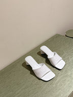 White slide sandals with embossed Balenciaga logo and block heel, side by side