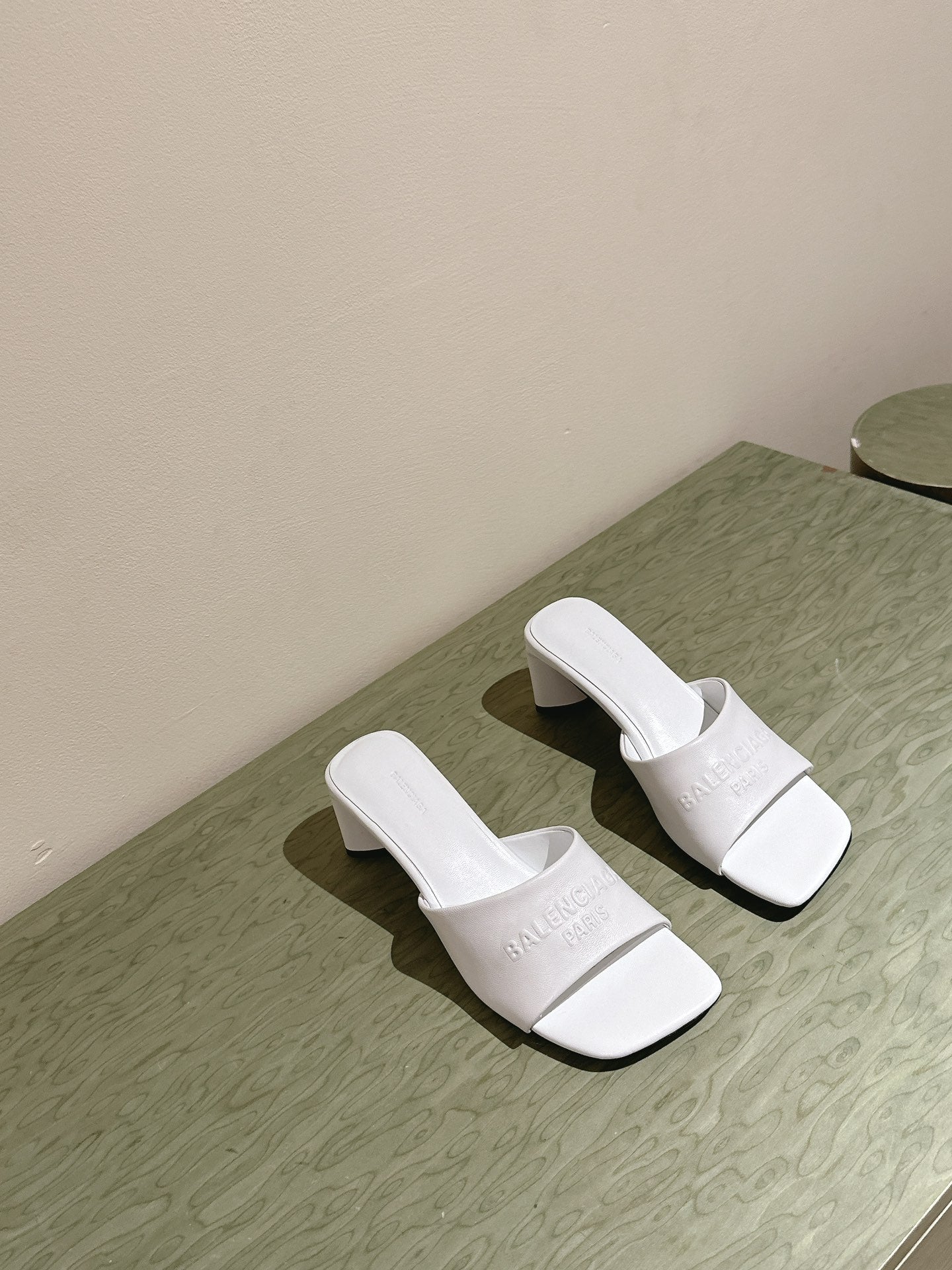 White slide sandals with embossed Balenciaga logo and block heel, side by side